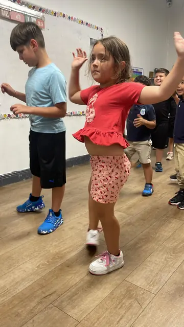 Niños bailan con los brazos en alto en una clase del After School