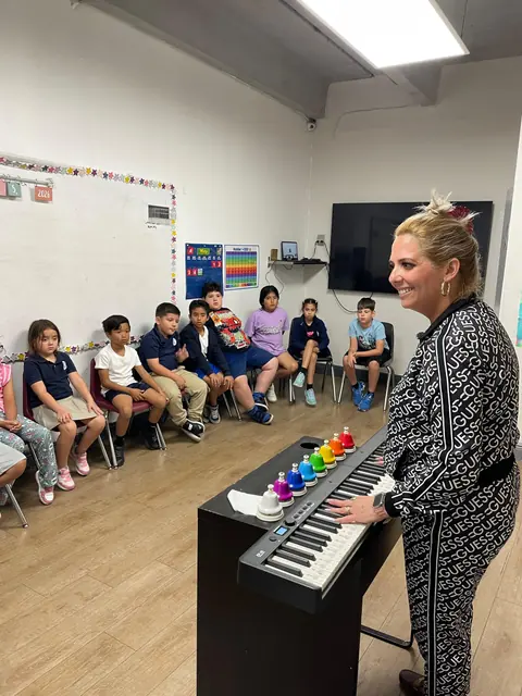 Una maestra toca un teclado y campanas de colores para un grupo de niños sentados