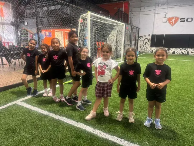 Niñas y niños con uniforme negro posan en una cancha de fútbol techada
