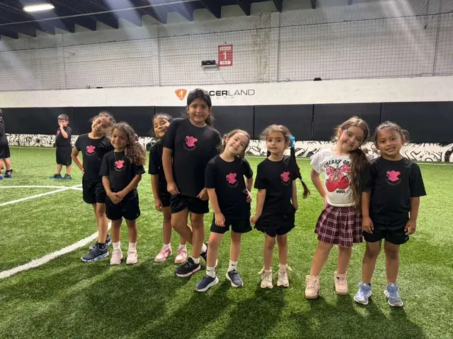 Un grupo de niños con camiseta negra sonríe en una cancha de fútbol techada