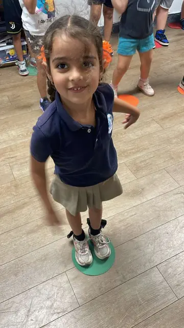 Una niña con uniforme sonríe mientras juega sobre un círculo de colores en el salón