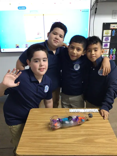 Cuatro estudiantes de primaria con uniforme azul posan juntos en su salón
