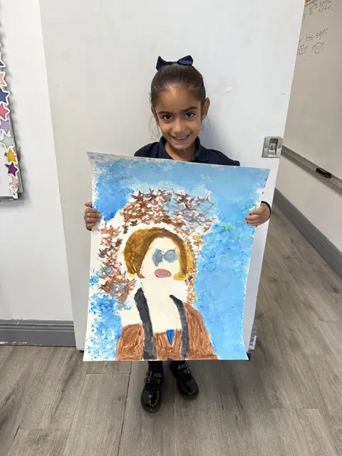 Una niña con uniforme muestra una pintura que hizo en clase de arte