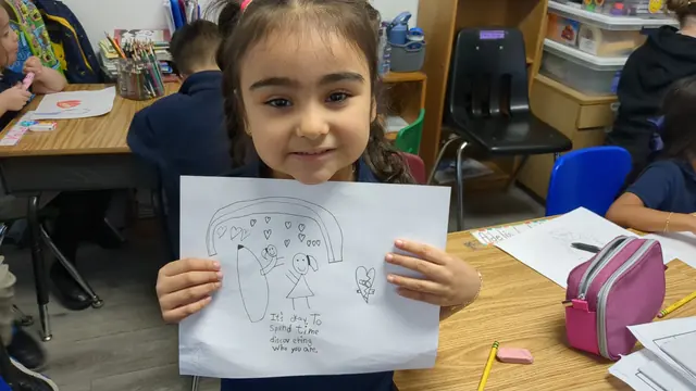 Una niña sonríe mientras muestra el dibujo que hizo en su salón