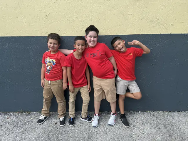 Cuatro estudiantes con camiseta roja posan de forma divertida junto a un muro