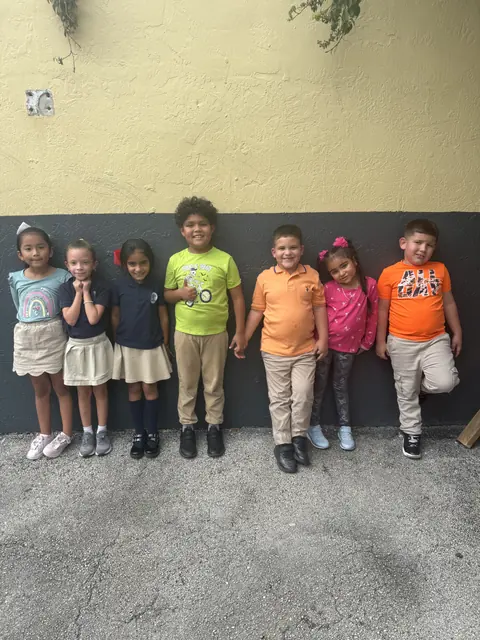 Un grupo de estudiantes de primaria posa en fila junto a un muro