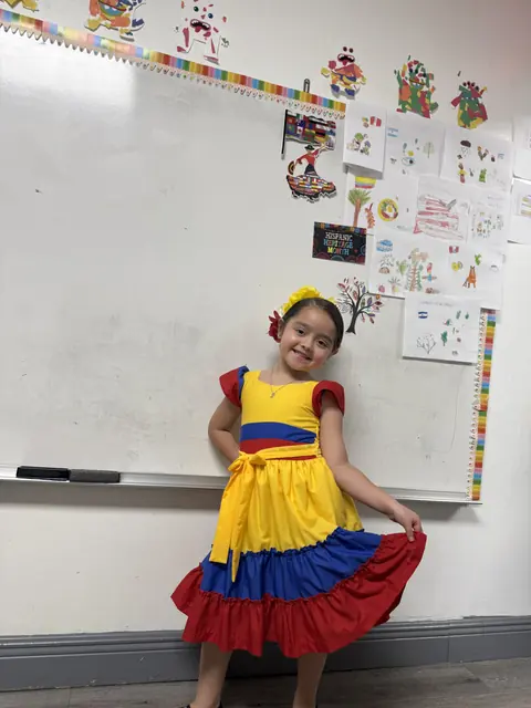 Una niña con un vestido típico amarillo, azul y rojo posa en su salón
