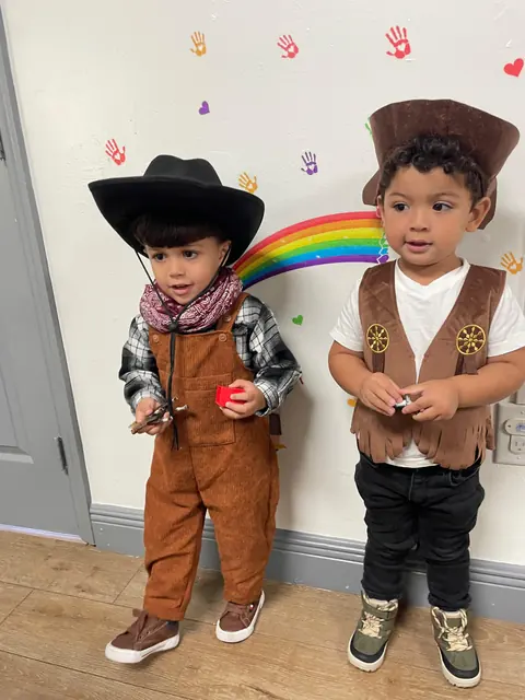 Dos niños pequeños disfrazados de vaqueros junto a un arcoíris pintado en la pared