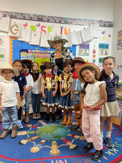 Niños y una maestra con sombreros de vaquero posan en un salón decorado