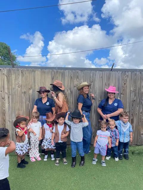 Maestras y niños con sombreros de vaquero posan en el patio bajo un cielo azul