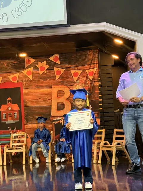 Un niño con toga y birrete azul recibe su diploma en el escenario de la graduación
