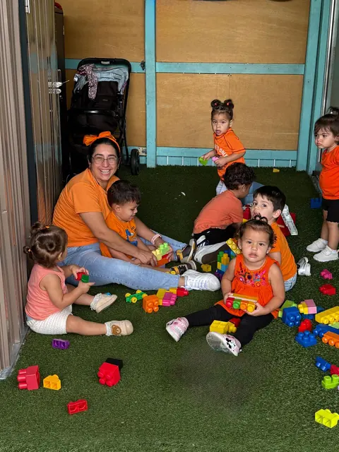 Una maestra y niños pequeños juegan con bloques de colores sobre el césped artificial
