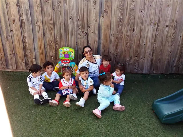 Una maestra y niños pequeños sentados en el patio junto a un tobogán